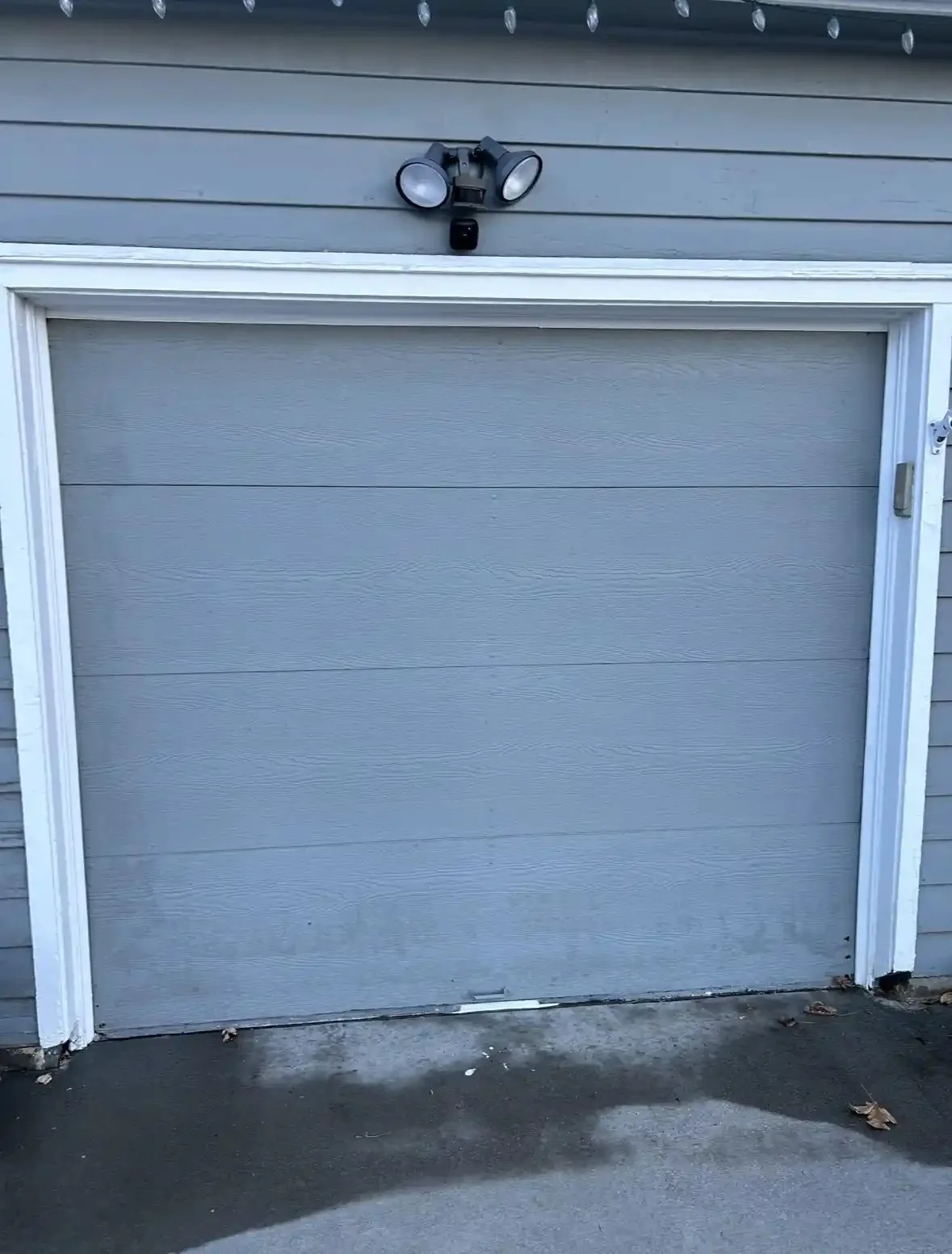 New gray single-car garage door on a blue-sided home